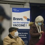 Trois personnes attendent près d'une pancarte où on peut lire : « Bravo, vous êtes maintenant vacciné! »