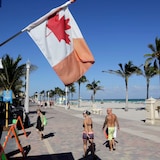 Isang Canadian flag lumilipad habang naglalakad ang mga tao sa boardwalk.