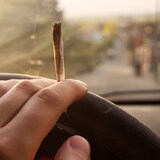 Une main tient un joint de cannabis et tient le volant d'une voiture. 