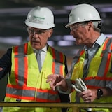 Mark Carney and another man speaking. They are both wearing hard hats and high-visibility vests.