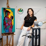 A woman poses between two paintings in similar styles.