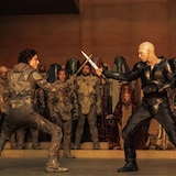 Deux hommes brandissant des épées se faisant face devant un public.