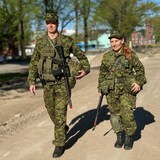 Un homme et une femme qui portent un treillis militaire et une arme en bandoulière marchent côte à côte.