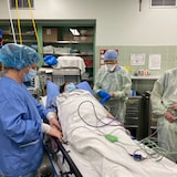 Una mujer yace en una cama de hospital en un quirófano, rodeada de personal médico.