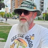 Dan Livers, chapeau et lunettes noires, regarde l'objectif.