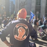 Un homme portant un chandail arborant un poing fermé avec le slogan « Les travailleurs debout »  devant le défilé de la fête du Travail à Toronto.