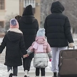 عائلة تجرّ حقيبة سفر عبر موقف سيارات مكسوٍّ بالثلوج.