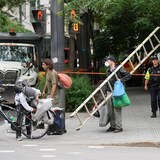 Des personnes, dont certaines masquées, portent leurs effets personnels après que la police a démantelé leur campement installé au square Victoria à Montréal.