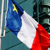 Drapeau acadien devant un édifice sur lequel est réfléchie la tour de Bell Aliant de Moncton.