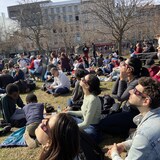 
أشخاص جالسون على العشب ويحملون نظارات كسوف الشمس وهم ينظرون إلى السماء.