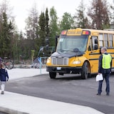 Une personne observe un parent avec son enfant marchant sur un trottoir, devant un autobus scolaire.