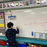 طفل يكتب باللغة العربية بقلم لبدي على سبورة بيضاء.