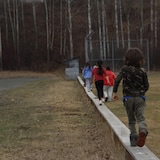 Des enfants de dos qui marchent en équilibre sur un muret.