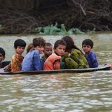 Des enfants assis dans une soucoupe flottent sur l'eau, poussés par un homme qui nage.