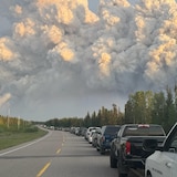 Un énorme nuage de fumée s'élève au-dessus d'une file de voitures sur l'autoroute 2 lors de l'évacuation de La Ronge, en Saskatchewan, en raison des feux de forêt, le 2 juin 2025.