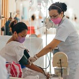 Isang babeng nars kinukuha ang blood pressure ng isang pasyenteng babae na nakasuwero sa loob ng ospital.