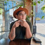JP Catungal nakasombrero at salamin at may hawak na tasa sa loob ng isang cafe.