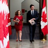 Chrystia Freeland and Justin Trudeau, all smiles, walk by a row of Canadian flags.