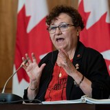 Portrait de la sénatrice Yvonne Boyer devant un drapeau canadien, en train de parler. 