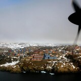 An aerial shot of the town of Sisimiut in the background, with a propeller plane nose shown in the foreground. 