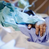 Un patient est dans un lit d'hôpital. Il y a un gros plan sur sa main.