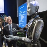 Federal Industry Minister Francois-Philippe Champagne laughs at a joke from an AI robot as Helene Desmarais, executive chairwoman, of IVADO Labs looks on at the All In artificial intelligence conference on Wednesday in Montreal. (Ryan Remiorz/The Canadian Press)