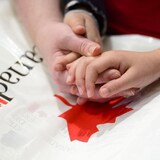 Des mains entrelacées sur un sac orné d'une feuille d'érable et du mot Canada.