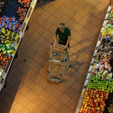 Isang mamimili na lalaki itinutulak ang shopping cart sa produce aisle.