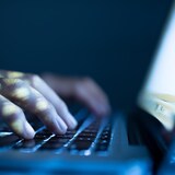 Les mains d'une personne sont posées sur le clavier d'un ordinateur portable dans l'obscurité.