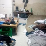 Une salle malpropre avec un matelas et des vêtements éparpillés.