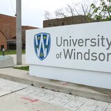 Un panneau de l'Université de Windsor avec un étudiant qui marche au loin.