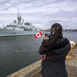 Una mujer sostiene una pequeña bandera canadiense mientras zarpa un barco militar.