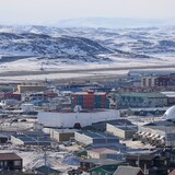Des maisons d'Iqaluit avec des montagnes à demi enneigées à l'arrière-plan.