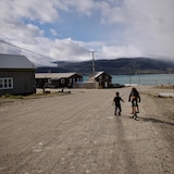 Une fillette fait de la bicyclette, et un garçon court à côté d'elle dans une rue de Pangnirtung, en août 2023.