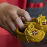 Une main tient de petits mocassins jaunâtres.
