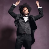 Un chef d'orchestre lève les bras et sa baguette dans les airs. 