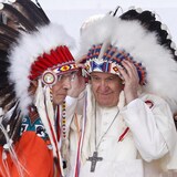 البابا فرنسيس (إلى اليمين) يعتمر غطاء رأس تقليدياً للسكان الأصليين تلقاه في نهاية خطابه في ماسكواسيس في ألبرتا في 25 تكموز (يوليو) 2022 في إطار زيارته إلى كندا.