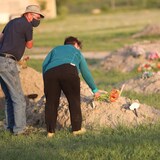 Dos personas dejan flores en una tumba sin marcar.