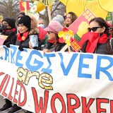 Mga babae hawak ang banner na nagsasabing 'Caregivers are Skilled Workers.'