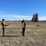 Deux employés d'AltoMaxx vêtu de vestes fluorescentes utilisent un drone dans la Première Nation de Pine Creek, au Manitoba, le 11 mai 2022.