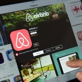 Un doigt touchant un écran sur lequel on voit la page d'accueil d'Airbnb.