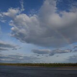 A river and forest landscape with a rainbow in the side. 