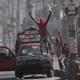 Un hombre con pasamontañas se tiene de pie sobre un coche en Haití.