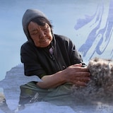 [ES] Mujer inuit con ropa oscura sentada al aire libre. Acaricia un objeto peludo (quizás una piel animal) bajo un cielo azul. Montaje con diseños etéreos.
[FR] Femme inuite assise en extérieur, en tenue sombre. Elle caresse un objet à fourrure sous un ciel bleu. Montage avec des motifs graphiques éthérés.