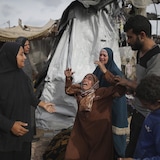 Une femme en pleurs au milieu d'autres personnes et d'un camp en ruines.