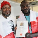 Razak Iyal, left, and Seidu Mohammed are draped in Canadian flags after they officially became citizens earlier this month. The two friends almost lost their lives as they walked across the U.S. border in the freezing cold to get to Canada, back in 2016. (Ian Froese/CBC)