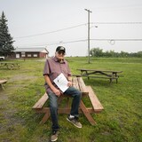 Un homme pose assis sur une table, un document en main.