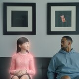 Un homme, assis sur un divan, regarde à sa gauche vers un avatar qui ressemble à une femme. 