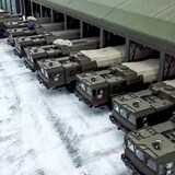 A dozen military tanks come out of a building.