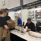 Un homme en train de signer un livre et en face de lui une femme et un homme.